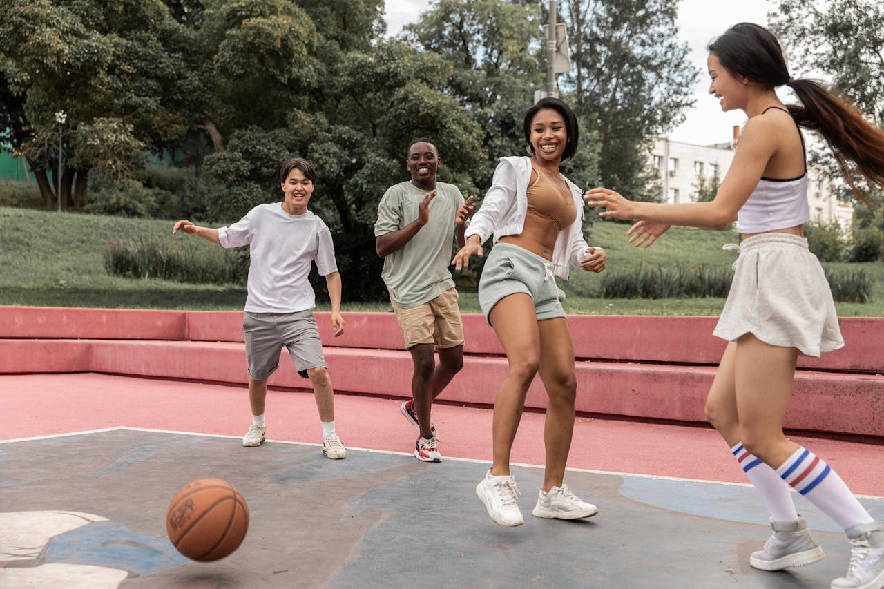 A group of diverse young adults playing basketball outdoors, laughing and having fun.